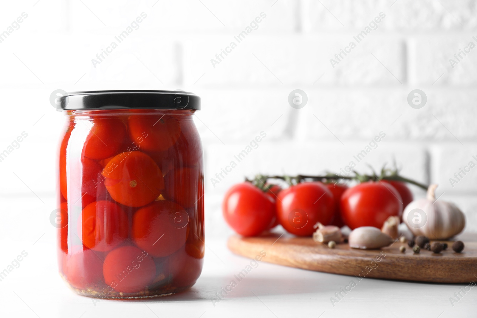 Photo of Tasty pickled tomatoes in jar, fresh vegetables and spices on white table