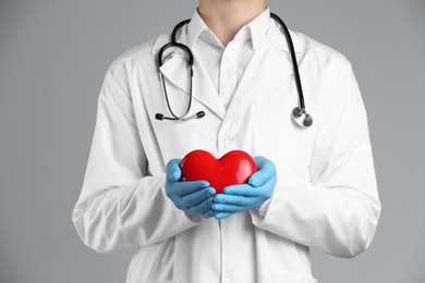 Doctor with red heart on grey background, closeup