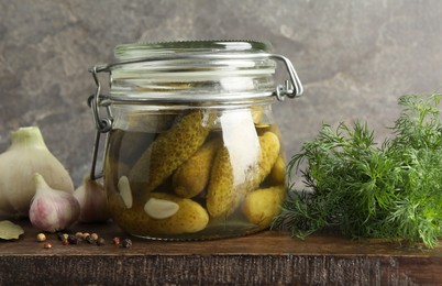 Pickled cucumbers in jar and spices on wooden table