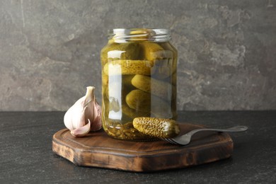 Pickled cucumbers in jar and garlic on grey table