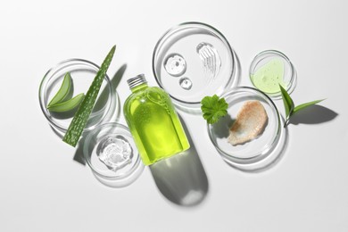 Photo of Petri dishes with different cosmetic products and aloe vera leaves on white background, flat lay