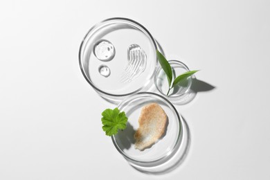 Petri dishes with different cosmetic products and leaves on white background, flat lay