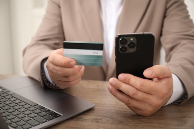 Photo of Man with credit card and smartphone at wooden table, closeup