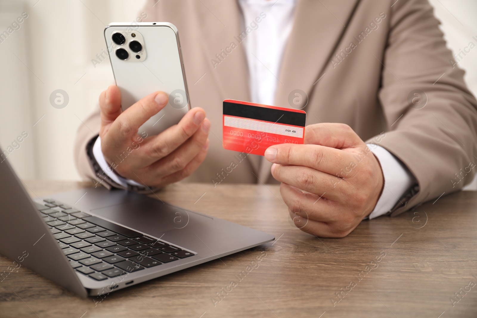 Photo of Man with credit card and smartphone at wooden table, closeup