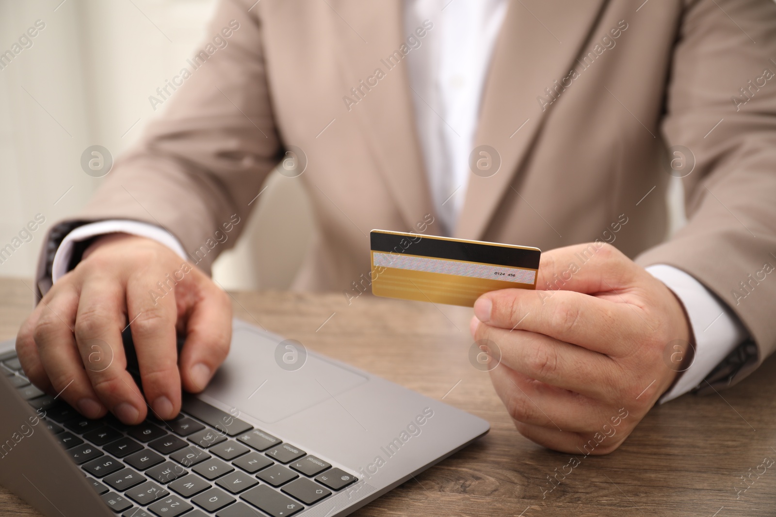 Photo of Man with credit card using laptop at wooden table, closeup