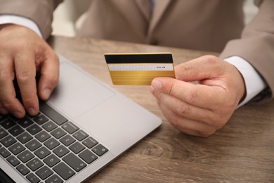 Photo of Man with credit card using laptop at wooden table, closeup