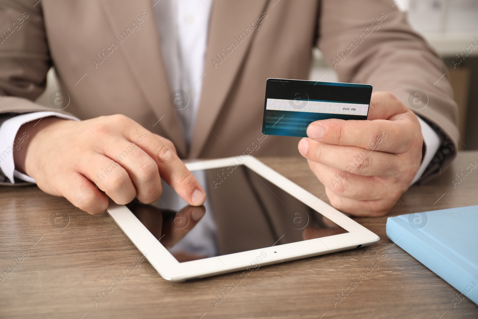 Photo of Man with credit card using tablet at wooden table, closeup