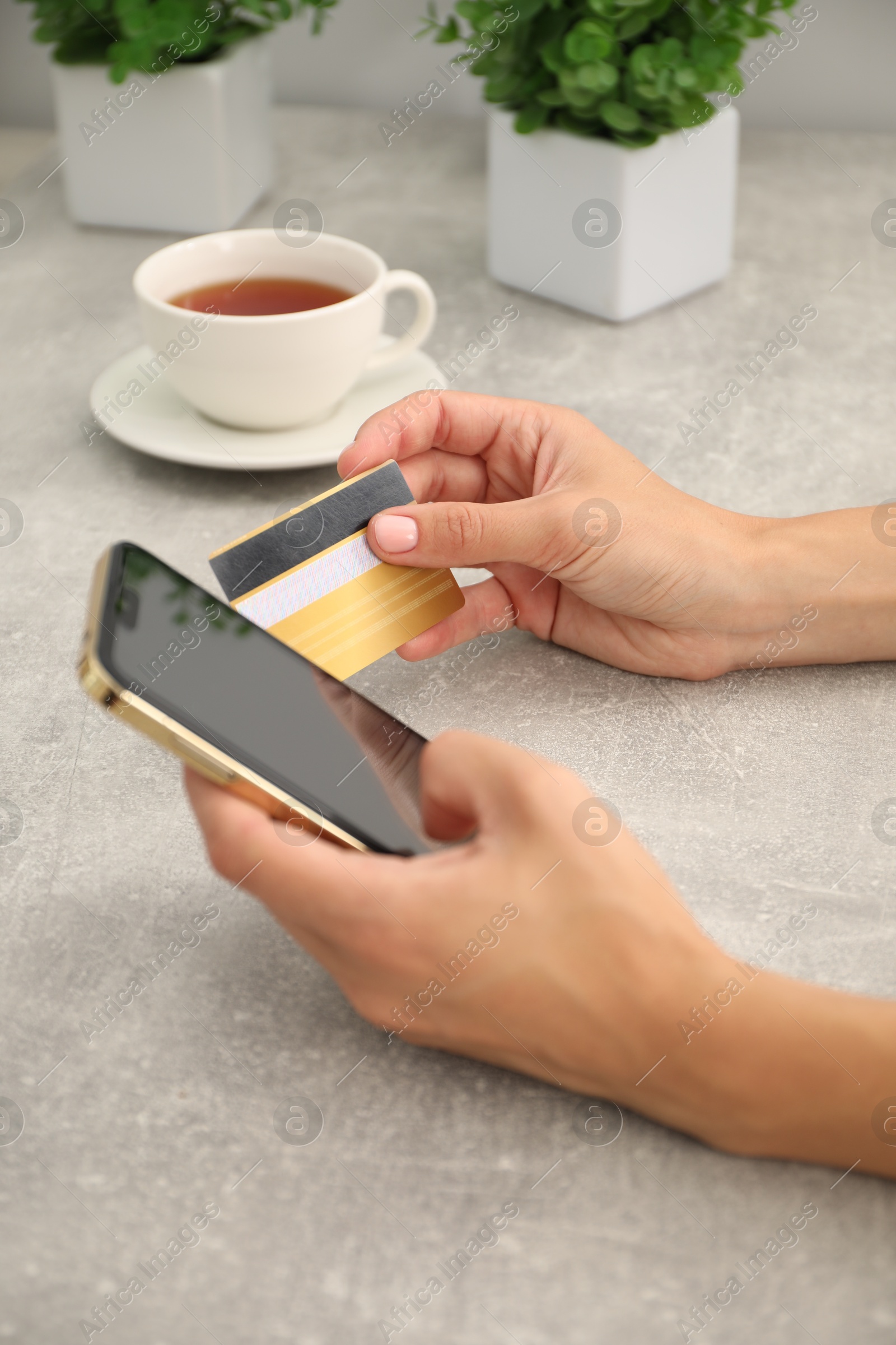 Photo of Woman with credit card using smartphone at gray textured table, closeup