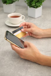 Photo of Woman with credit card using smartphone at gray textured table, closeup