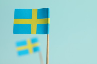 Small paper flags of Sweden on light blue background, selective focus. Space for text