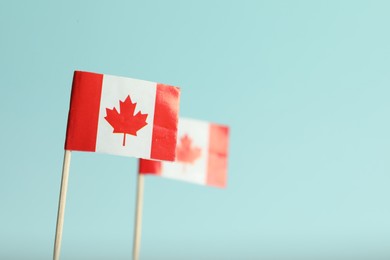 Photo of Small paper flags of Canada on light blue background, selective focus. Space for text