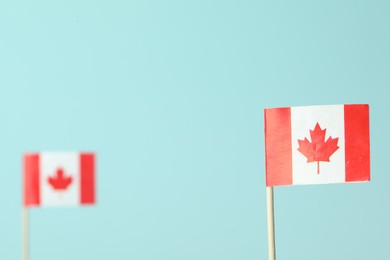 Small paper flags of Canada on light blue background, selective focus. Space for text