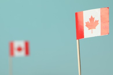 Photo of Small paper flags of Canada on light blue background, selective focus. Space for text