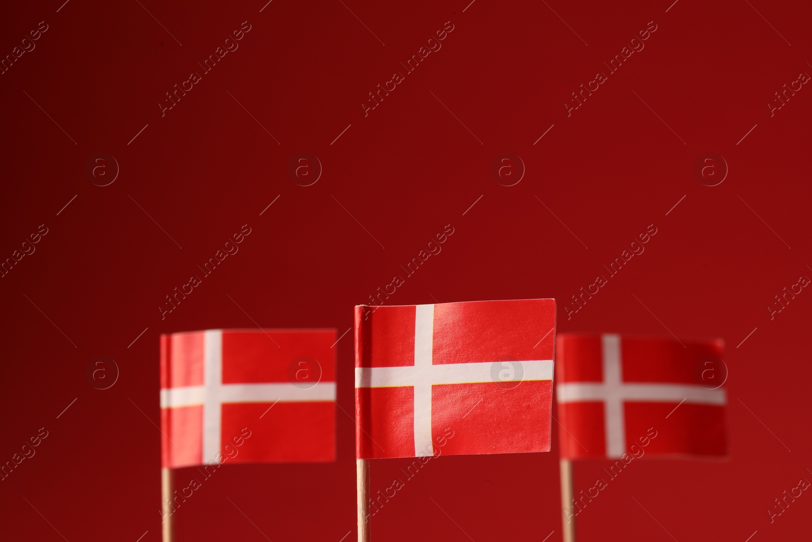 Photo of Small paper flags of Denmark on red background, selective focus. Space for text