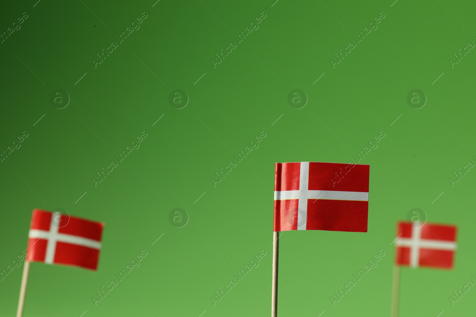 Photo of Small paper flags of Denmark on green background, selective focus. Space for text