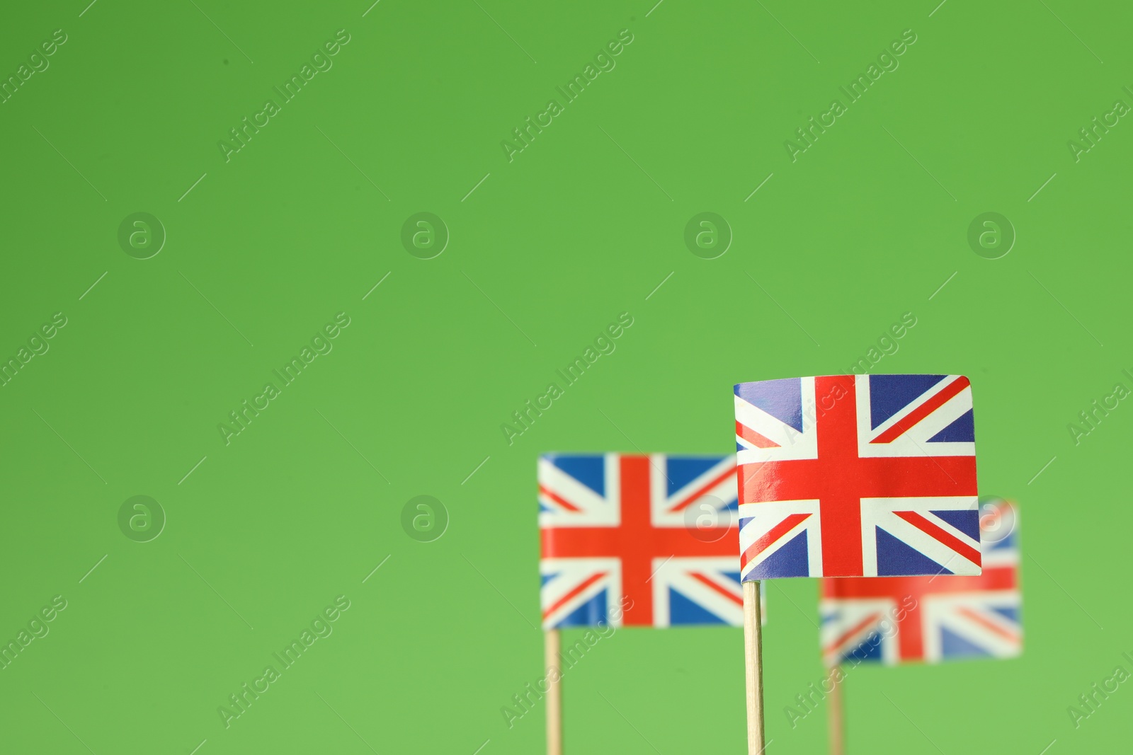 Photo of Small paper flags of United Kingdom on green background, selective focus. Space for text