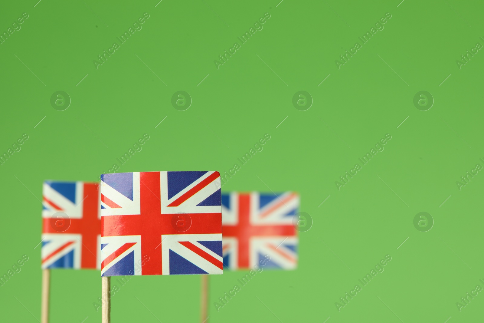 Photo of Small paper flags of United Kingdom on green background, selective focus. Space for text