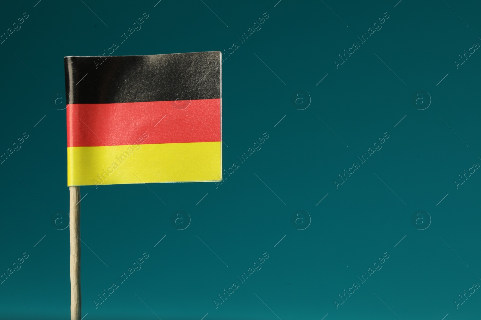 Photo of Small paper flag of Germany on teal background, closeup. Space for text