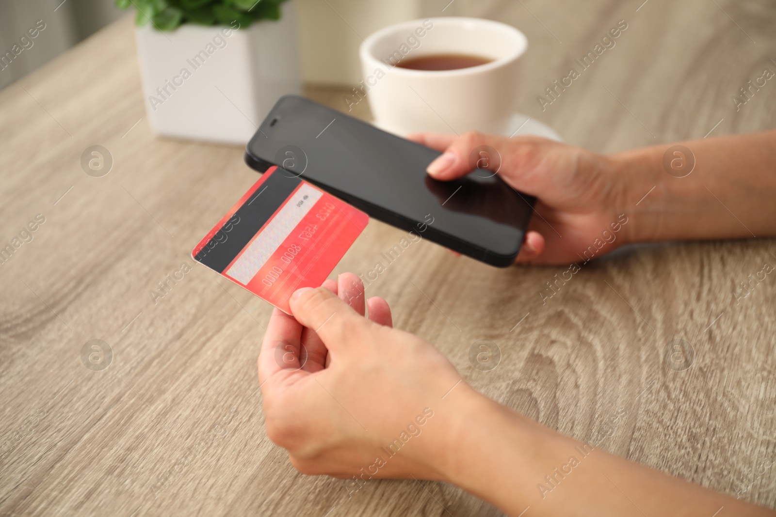 Photo of Woman with credit card using smartphone at wooden table, closeup