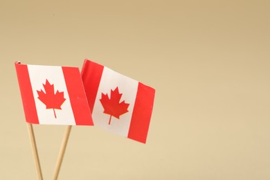 Small paper flags of Canada on beige background, closeup. Space for text