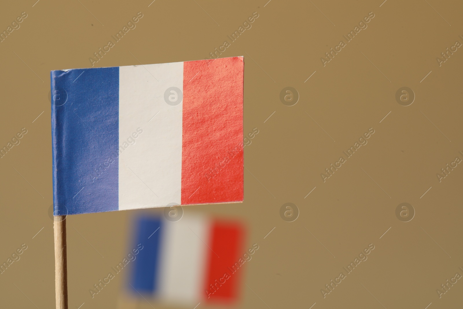 Photo of Small paper flags of France on beige background, selective focus. Space for text