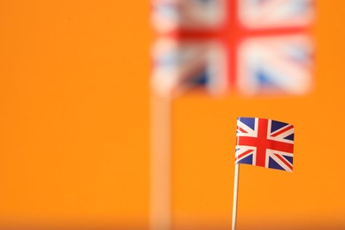 Photo of Small paper flags of United Kingdom on orange background, selective focus. Space for text