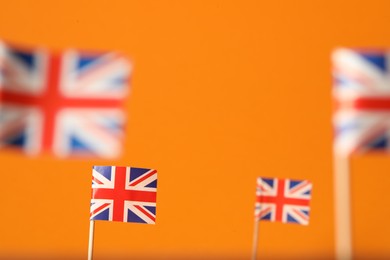 Photo of Small paper flags of United Kingdom on orange background, selective focus. Space for text