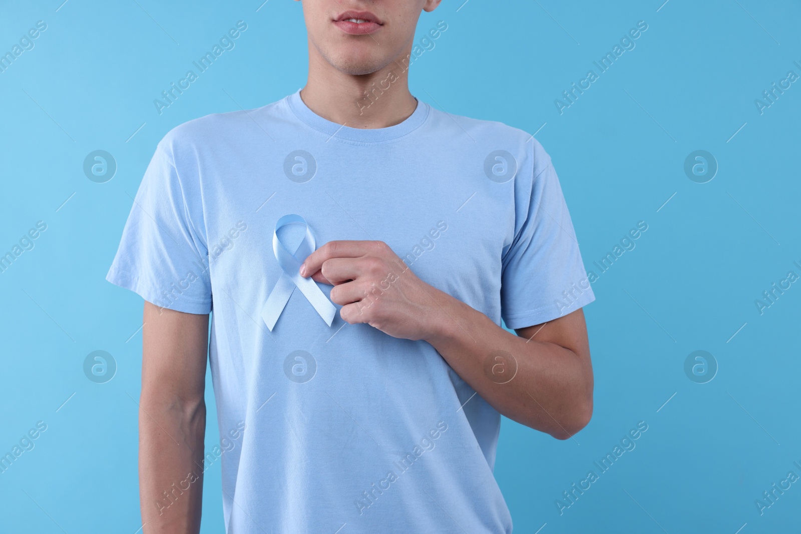 Photo of Prostate cancer awareness. Man with light blue ribbon as symbol of support on color background, closeup