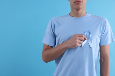 Prostate cancer awareness. Man with light blue ribbon as symbol of support on color background, closeup. Space for text