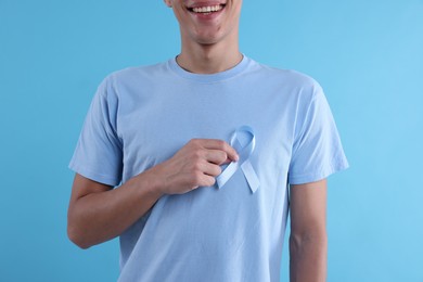 Photo of Prostate cancer awareness. Man with light blue ribbon as symbol of support on color background, closeup