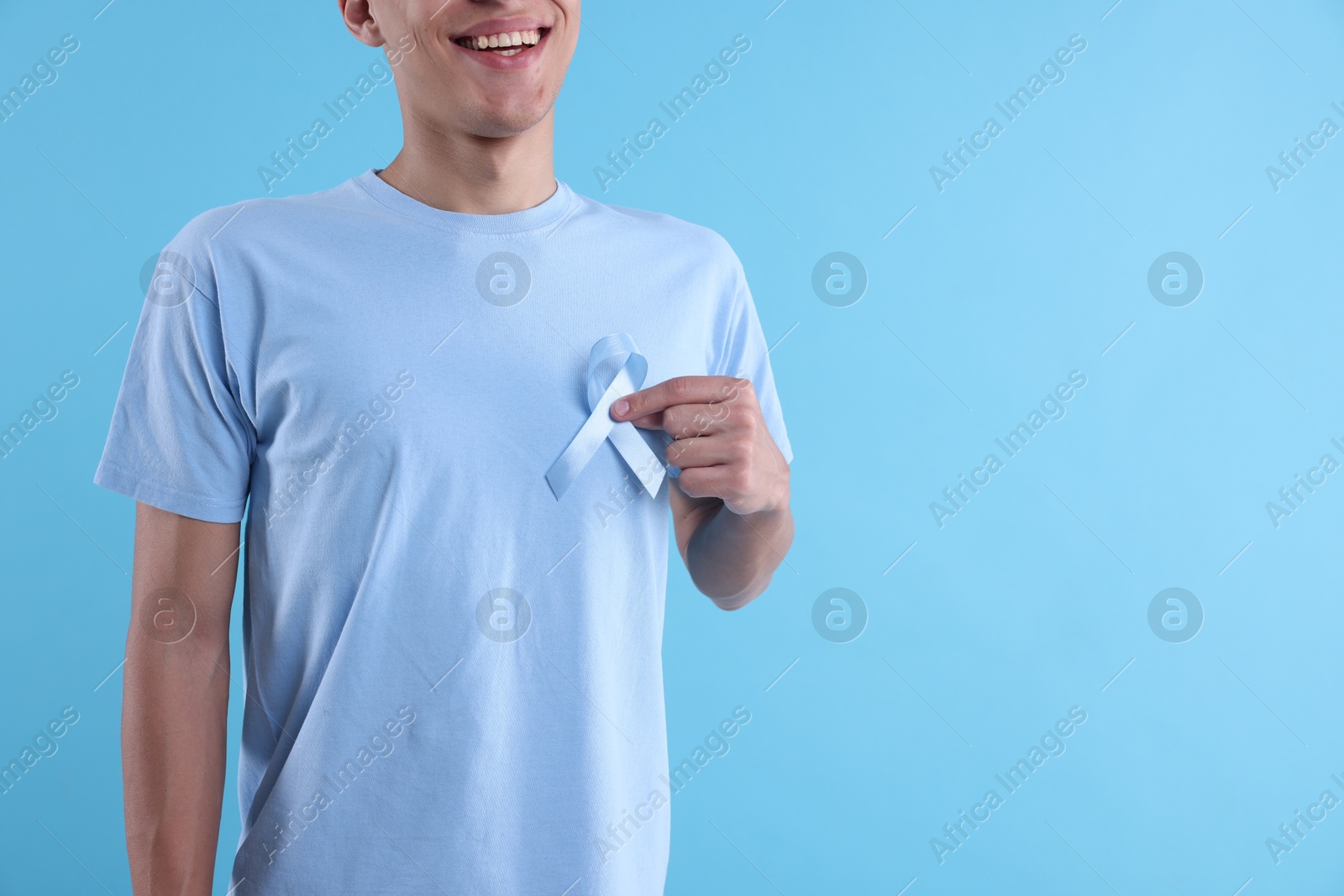 Photo of Prostate cancer awareness. Man with light blue ribbon as symbol of support on color background, closeup. Space for text