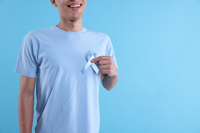 Photo of Prostate cancer awareness. Man with light blue ribbon as symbol of support on color background, closeup. Space for text