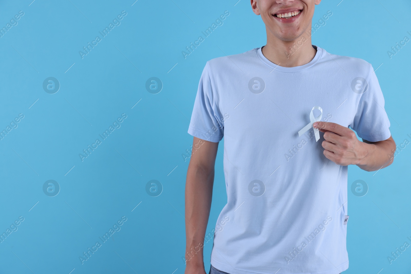 Photo of Prostate cancer awareness. Man with light blue ribbon as symbol of support on color background, closeup. Space for text