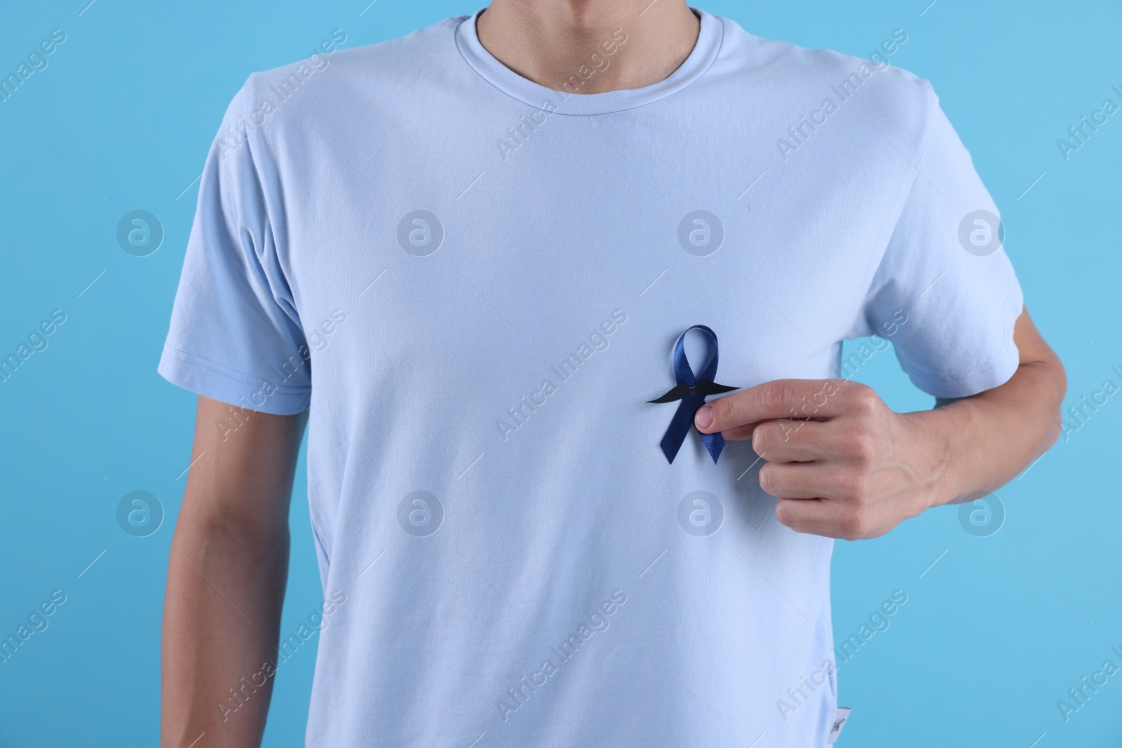 Photo of Prostate cancer awareness. Man with blue ribbon and fake mustache on color background, closeup