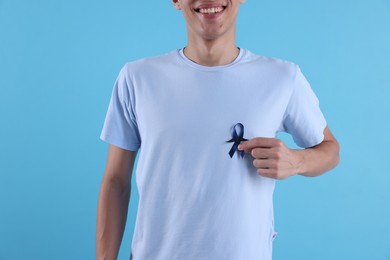 Prostate cancer awareness. Man with blue ribbon and fake mustache on color background, closeup