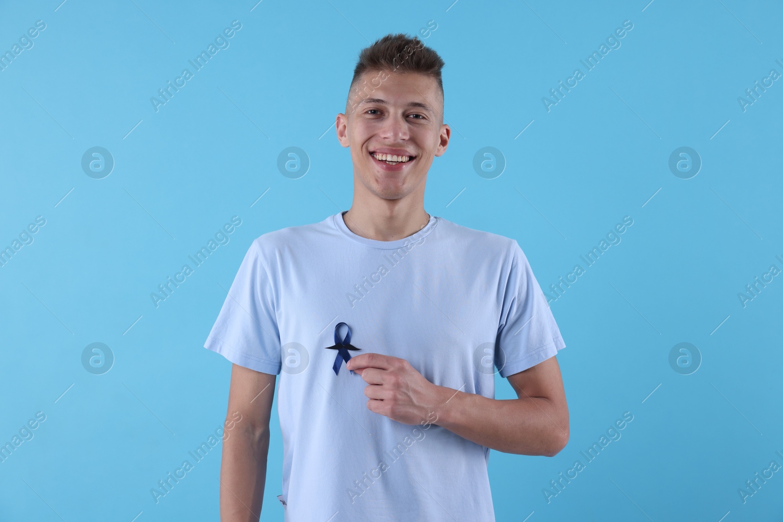 Photo of Prostate cancer awareness. Man with blue ribbon and fake mustache on color background