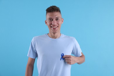 Photo of Prostate cancer awareness. Man with blue ribbon as symbol of support on color background