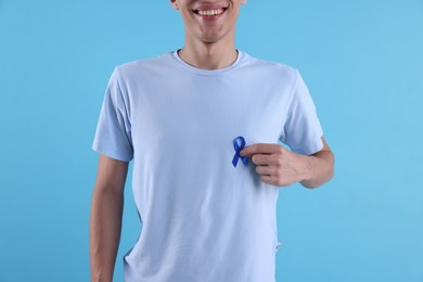 Prostate cancer awareness. Man with blue ribbon as symbol of support on color background, closeup