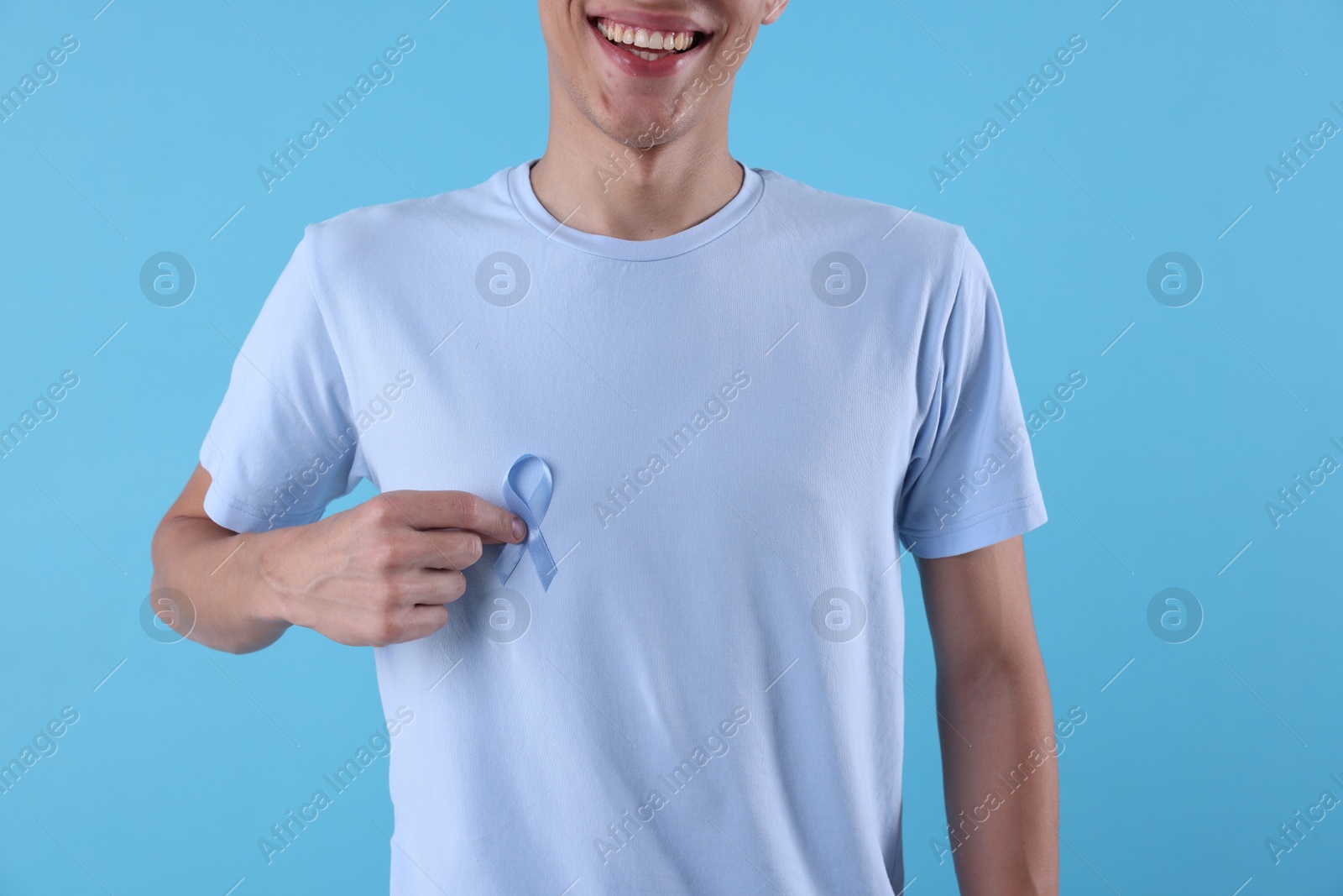 Photo of Prostate cancer awareness. Man with light blue ribbon as symbol of support on color background, closeup