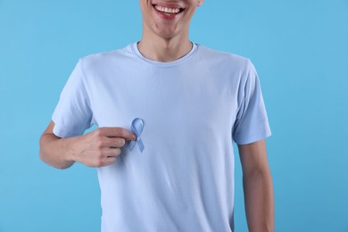 Prostate cancer awareness. Man with light blue ribbon as symbol of support on color background, closeup