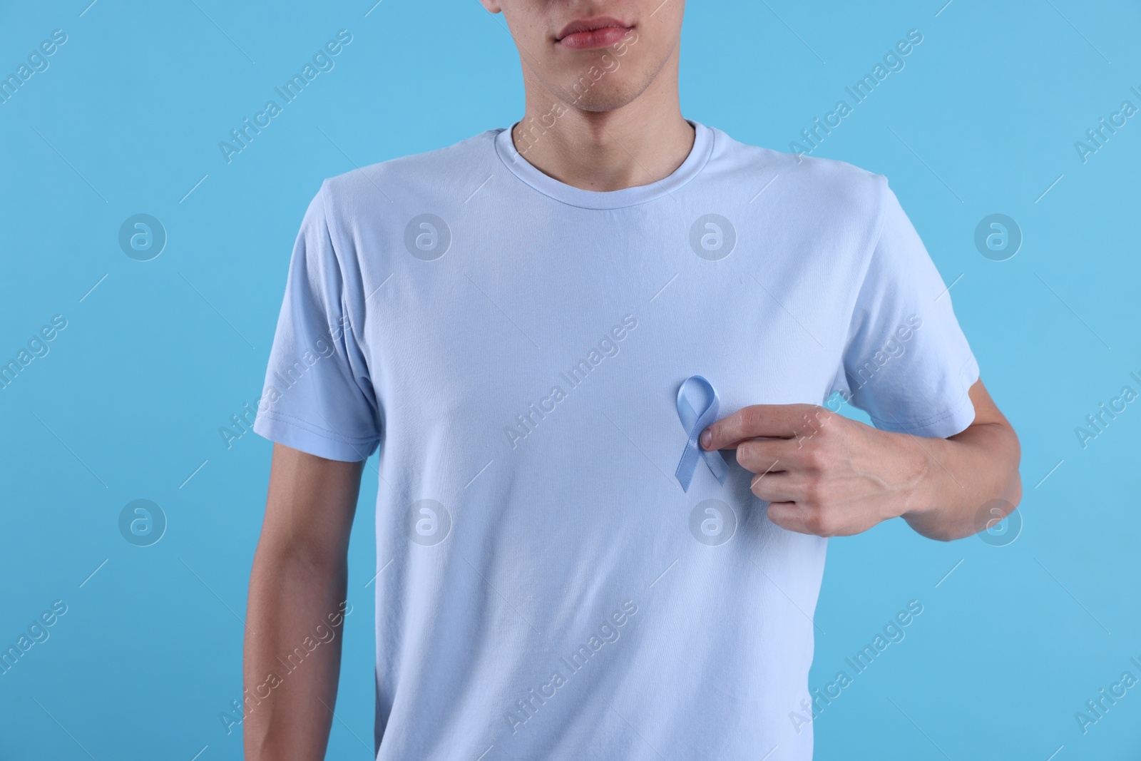 Photo of Prostate cancer awareness. Man with light blue ribbon as symbol of support on color background, closeup