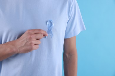 Photo of Prostate cancer awareness. Man with light blue ribbon as symbol of support on color background, closeup