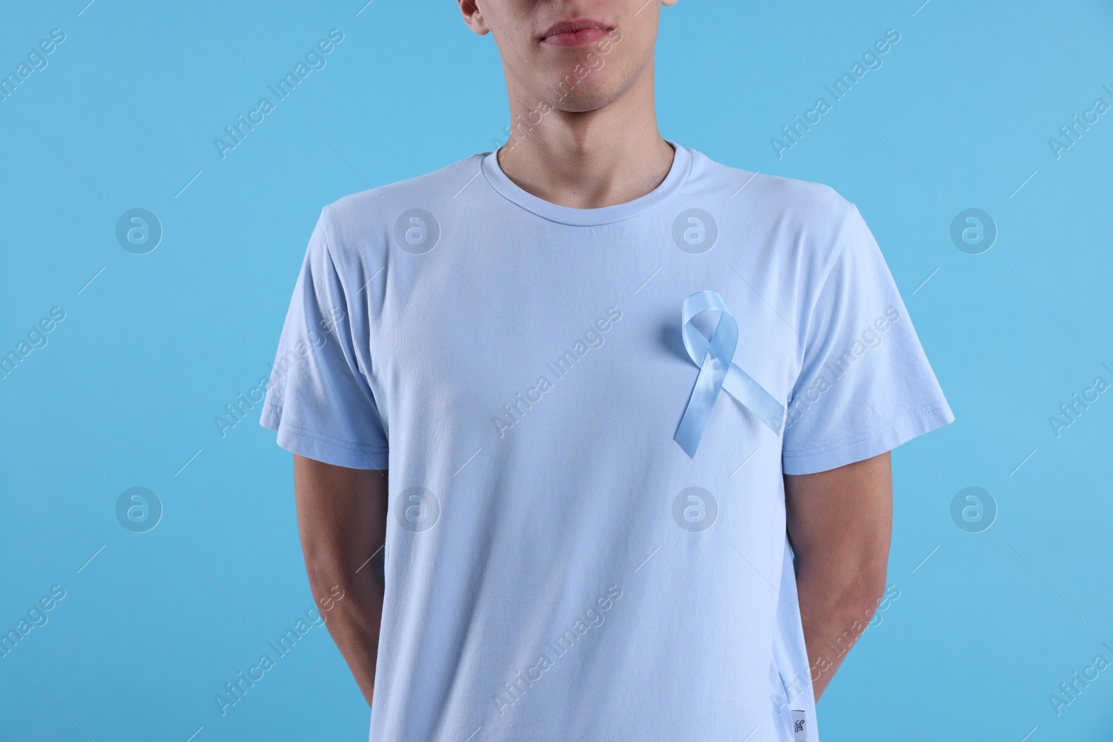 Photo of Prostate cancer awareness. Man with light blue ribbon as symbol of support on color background, closeup