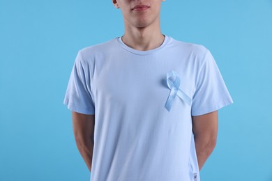 Prostate cancer awareness. Man with light blue ribbon as symbol of support on color background, closeup