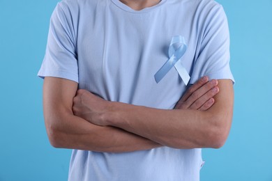 Photo of Prostate cancer awareness. Man with light blue ribbon as symbol of support on color background, closeup