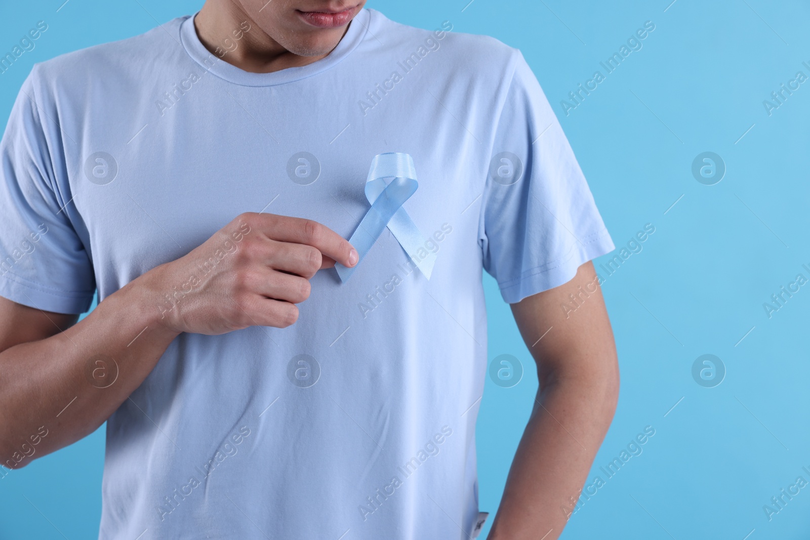 Photo of Prostate cancer awareness. Man with light blue ribbon as symbol of support on color background, closeup