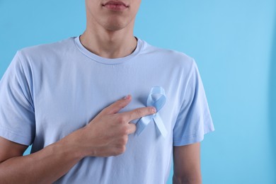 Prostate cancer awareness. Man with light blue ribbon as symbol of support on color background, closeup