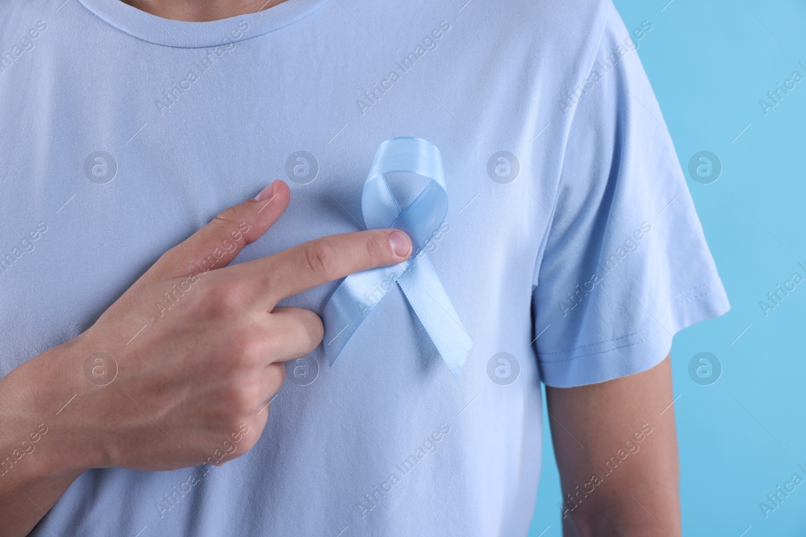 Photo of Prostate cancer awareness. Man with light blue ribbon as symbol of support on color background, closeup