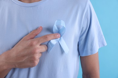 Photo of Prostate cancer awareness. Man with light blue ribbon as symbol of support on color background, closeup