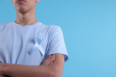 Photo of Prostate cancer awareness. Man with light blue ribbon as symbol of support on color background, closeup. Space for text